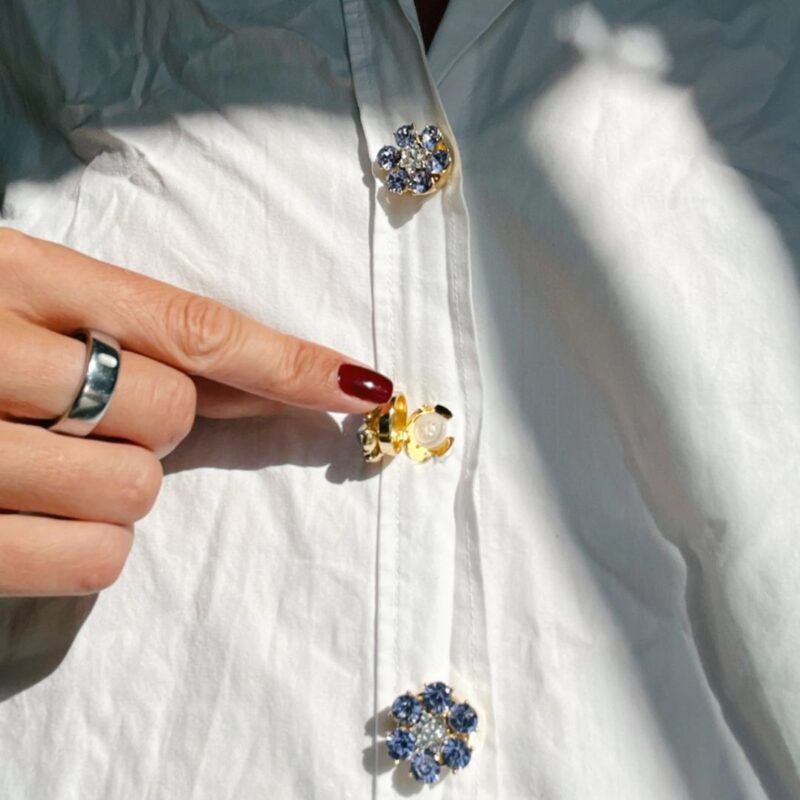 Named after the founder’s oma Hildegard, Hilde combines softness, elegance and personality in one refined accessory. Unlike traditional brooches or pins, these button charms simply click onto existing buttons up to 13 mm wide. No sewing and no permanent changes — just an effortless way to elevate shirts, blazers, cardigans or jackets within seconds. And honestly? They feel less like accessories and more like jewellery for your clothes.